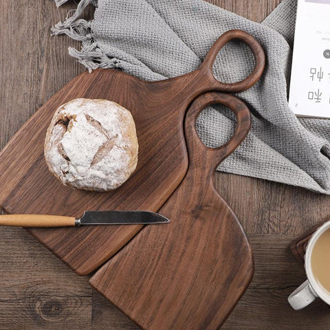 Walnut cutting boards on a table with a loaf of bread and a knife